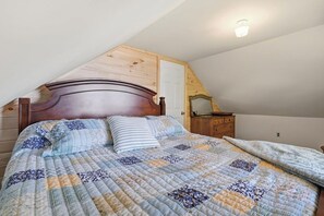 Une chambre avec un plafond en pente, une tête de lit en bois, une couvre-lit matelassé et une table de chevet avec un miroir.
