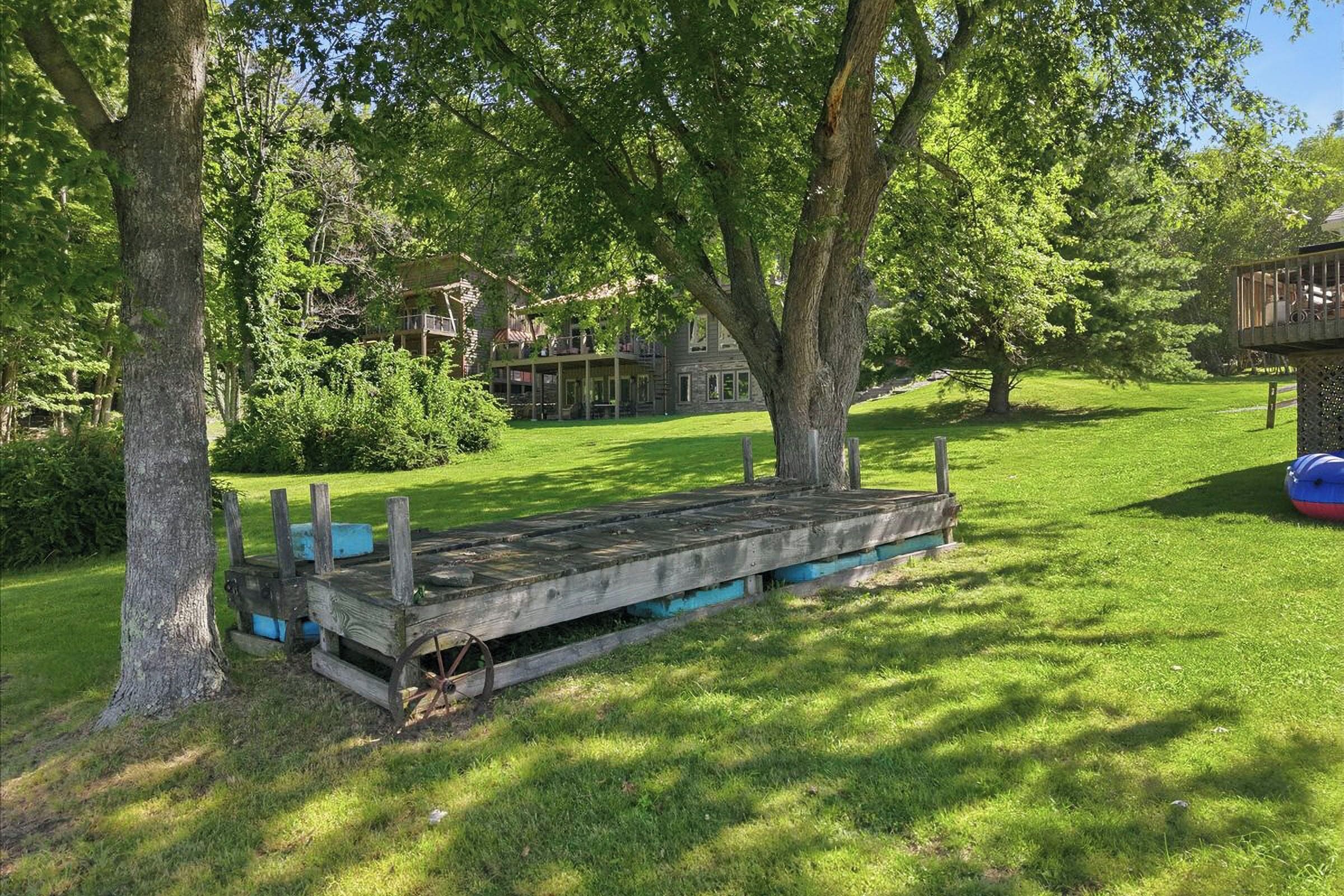 A wooden dock extending into a grassy area with trees and a house in the background.