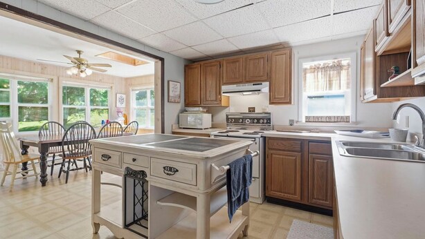 A kitchen with wooden cabinets, a stove, a sink, and a dining area with chairs and a table. - Lakefront Paradise on Lake Wallenpaupack w/ Dock (Hawley)