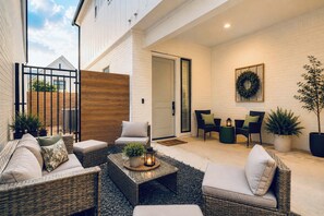 A covered outdoor seating area with wicker furniture, a small table with a candle, and a potted plant. - Magnolia Manor at College Station & Texas A&M (College Station)