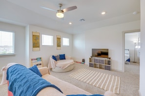 A modern living room with a ceiling fan, a flat-screen TV, and a bookshelf. - Fenced Yard! Family Getaway, Near Texas Ski Ranch (San Marcos)