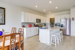 A modern kitchen with white cabinetry, a central island with stools, a microwave, and a stainless steel refrigerator. - Fenced Yard! Family Getaway, Near Texas Ski Ranch (San Marcos)