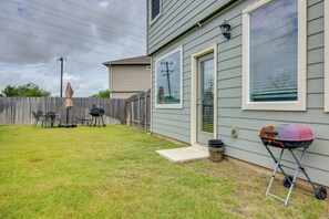 Un jardin arrière aménagé avec une pelouse, un barbecue, du mobilier d’extérieur et une clôture en bois.