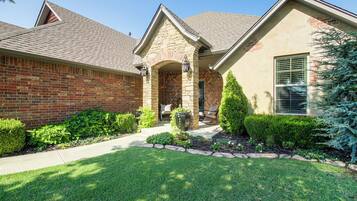 A residential house with a brick facade, a stone archway entrance, and a well-maintained front yard with a lawn and shrubs.