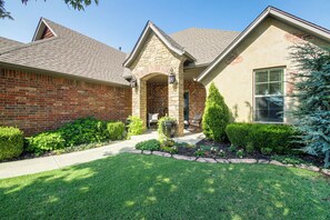 A residential house with a brick facade, a stone archway entrance, and a well-maintained front yard with a lawn and shrubs.