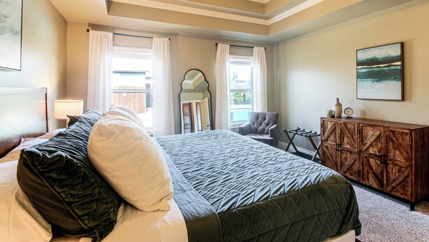 A hotel room with a bed, a chair, a wooden cabinet, and a painting on the wall. - Gateway to Downtown Okc! Elegant Home (Yukon)