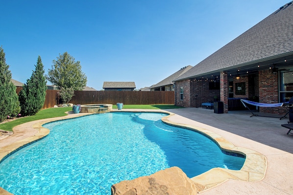 A backyard with a swimming pool, a barbecue area, and a brick building.