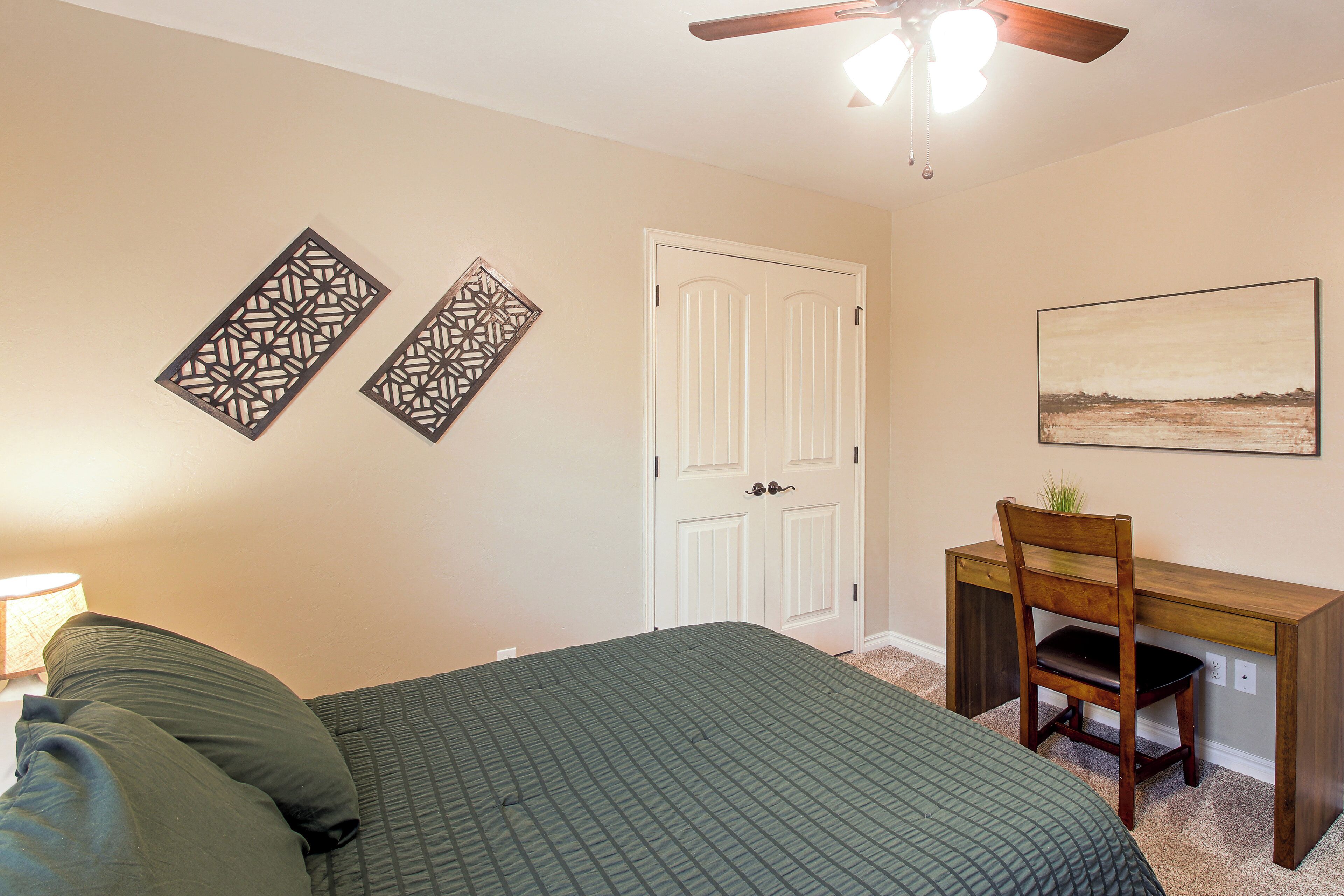 A bedroom with a bed, a desk, a chair, a door, and a wall-mounted picture.