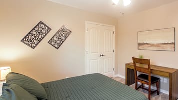 A bedroom with a bed, a desk, a chair, a door, and a wall-mounted picture.