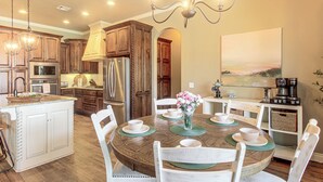 A modern kitchen with a central island, stainless steel appliances, and a dining area with a round table and chairs. - Gateway to Downtown Okc! Elegant Home (Yukon)