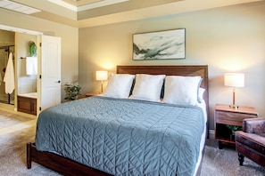 A bedroom with a large bed, two bedside lamps, a headboard, and a painting on the wall.