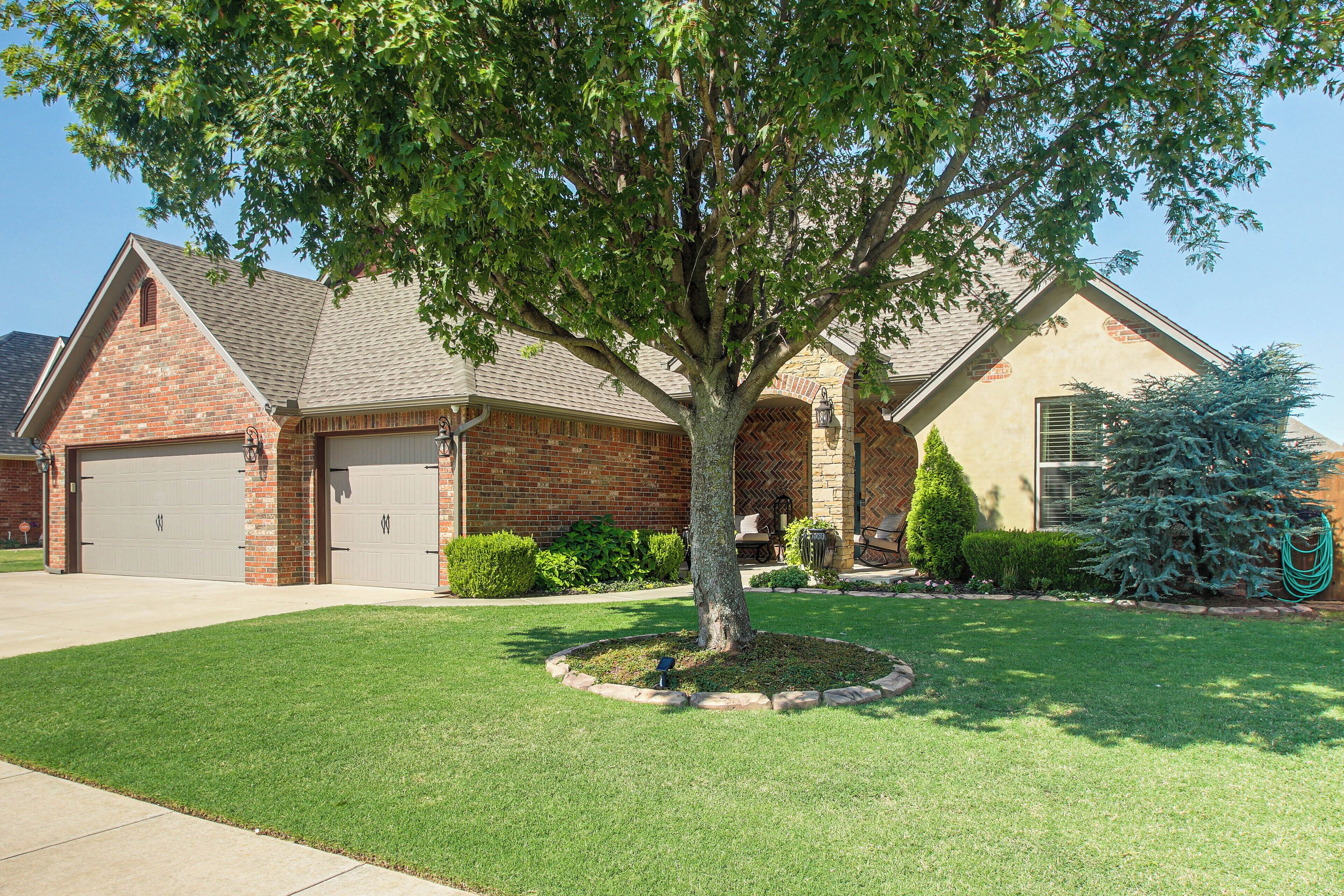 A residential property with a brick garage, a stone patio, and a well-maintained lawn.