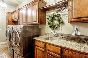 A kitchen with wooden cabinets, a stainless steel refrigerator, a granite countertop, a sink, and a wall-mounted drying rack. - Gateway to Downtown Okc! Elegant Home (Yukon)