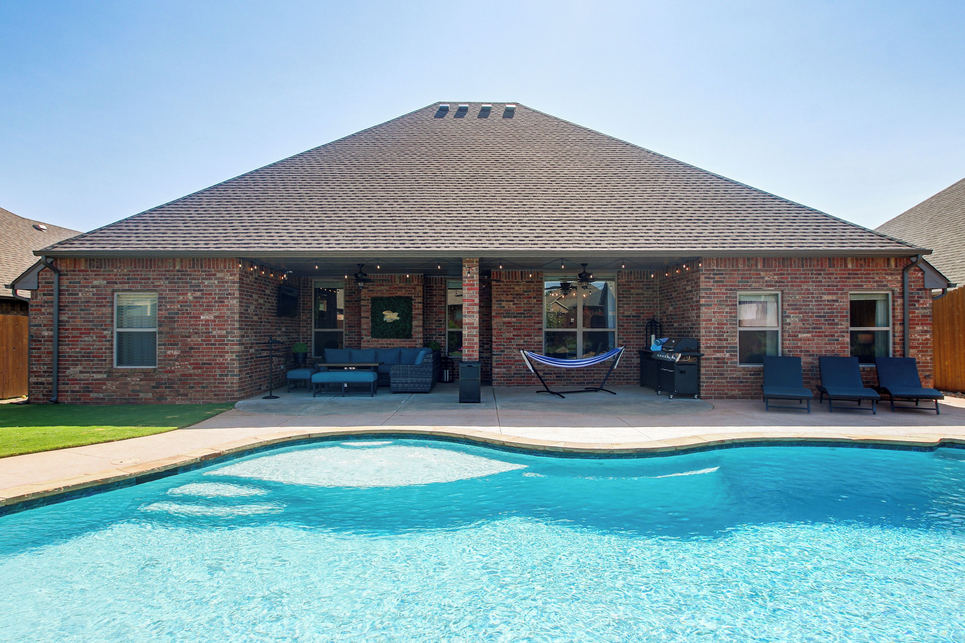 A brick house with a swimming pool, outdoor seating, and a hammock.