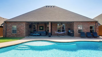 A brick house with a swimming pool, outdoor seating, and a hammock.