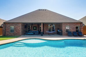 A brick house with a swimming pool, outdoor seating, and a hammock.