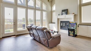 Ein geräumiges Wohnzimmer mit Ledersessel, Kamin und großem Fenster mit Blick auf einen Garten.