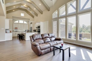 A spacious living area with a leather sofa, a coffee table, and a large window offering a view of the backyard.
