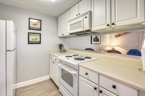 Una cocina con armarios blancos, una estufa y un refrigerador. Se observan cuadros en la pared.