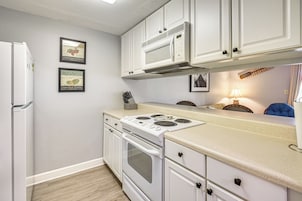 Una cocina con armarios blancos, una estufa y un refrigerador. Se observan cuadros en la pared.