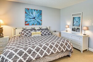 Un dormitorio con cama, dos mesitas de noche, cómoda y un cuadro grande con motivos florales en la pared.