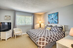 Habitación de hotel con cama, televisión, una silla, una lámpara y un cuadro en la pared.