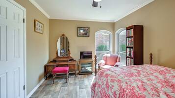 Une chambre à coucher comprenant un lit, une commode, une coiffeuse, un téléviseur, une bibliothèque et une fenêtre donnant sur un immeuble en briques.