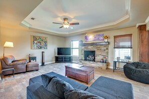 A living room with a fireplace, a ceiling fan, and a flat-screen TV. - Swim, Grill & Relax! Copperas Cove Family Home (Copperas Cove)