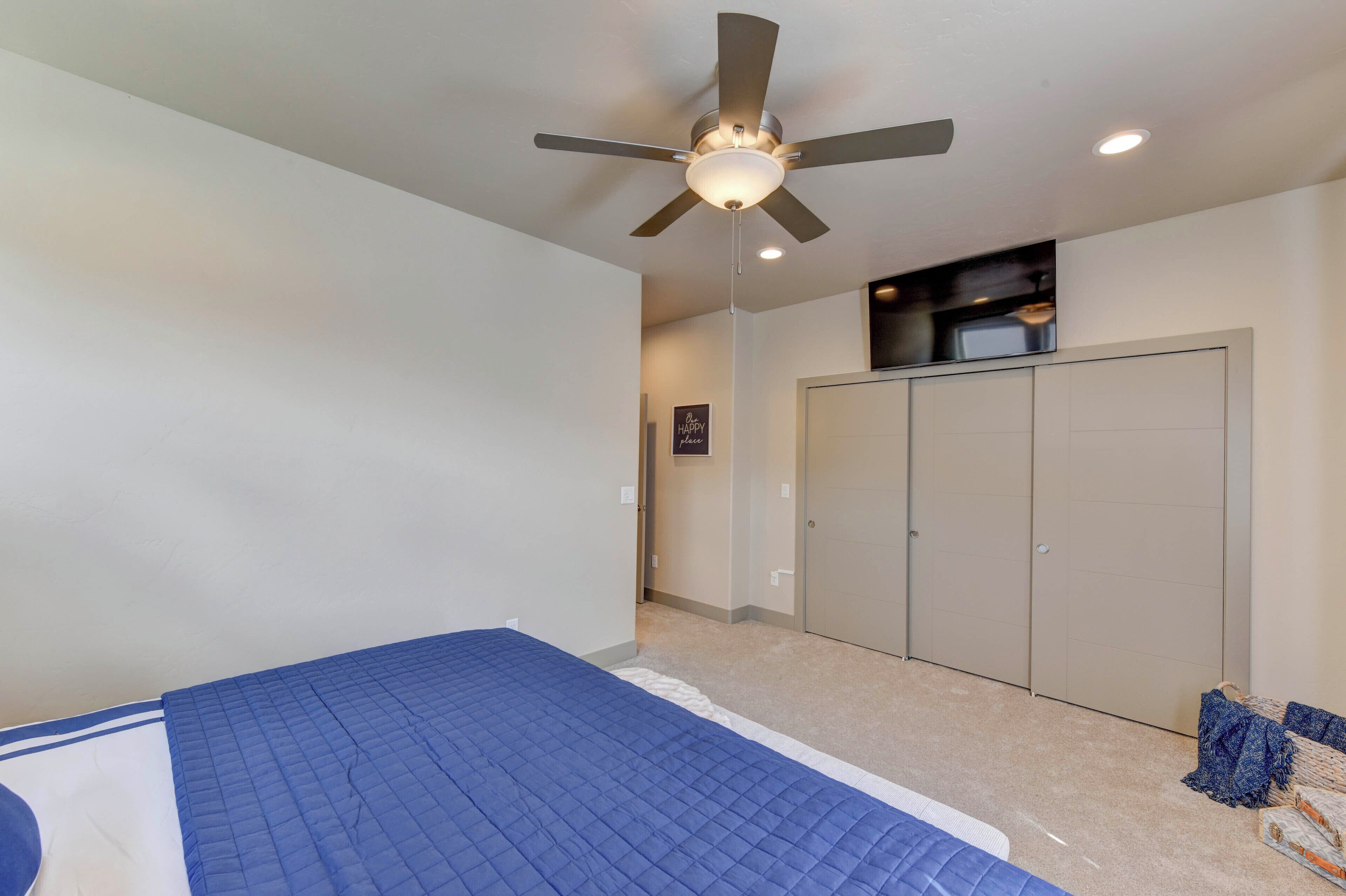 A bedroom with a bed, a ceiling fan, a wardrobe, and a television mounted on the wall.
