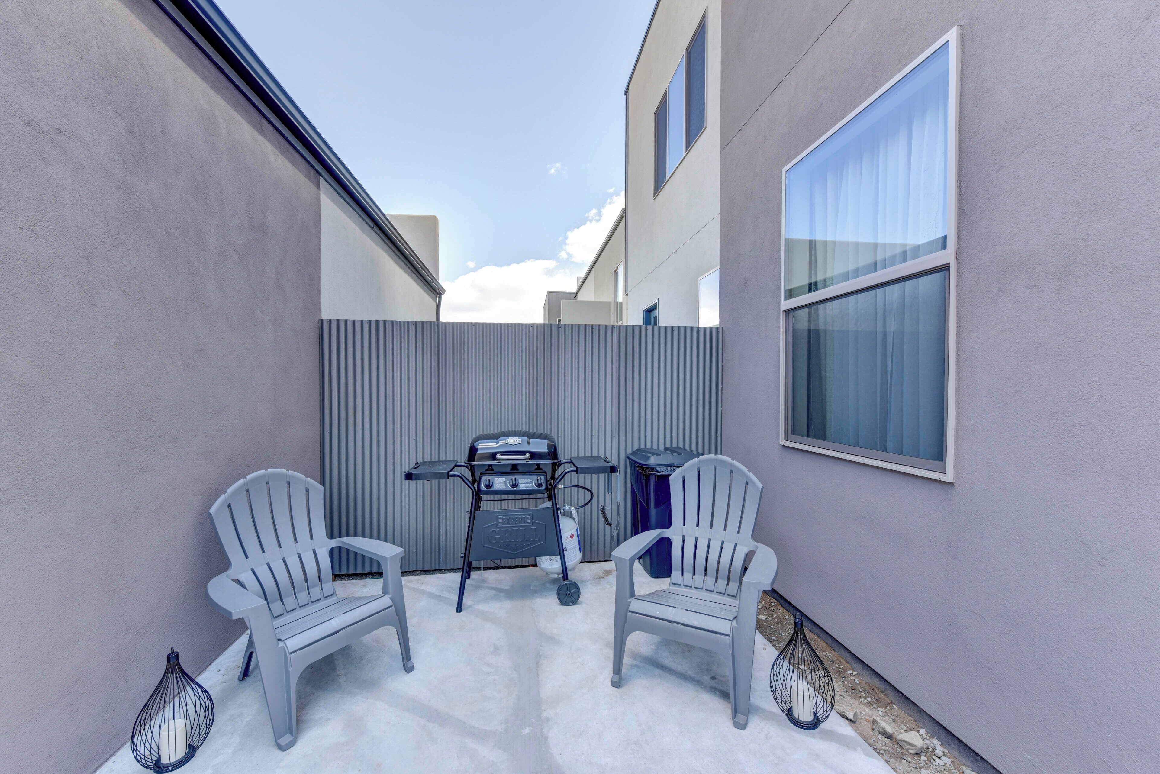 Une terrasse avec deux chaises, un barbecue et une fenêtre.