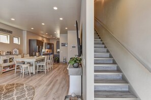 Uma cozinha ampla com eletrodomésticos modernos, uma área de refeições com mesa e cadeiras de madeira, e uma escada com design minimalista.