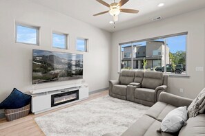 Ein modernes Wohnzimmer mit Flachbildfernseher, Deckenventilator und großem Fenster.
