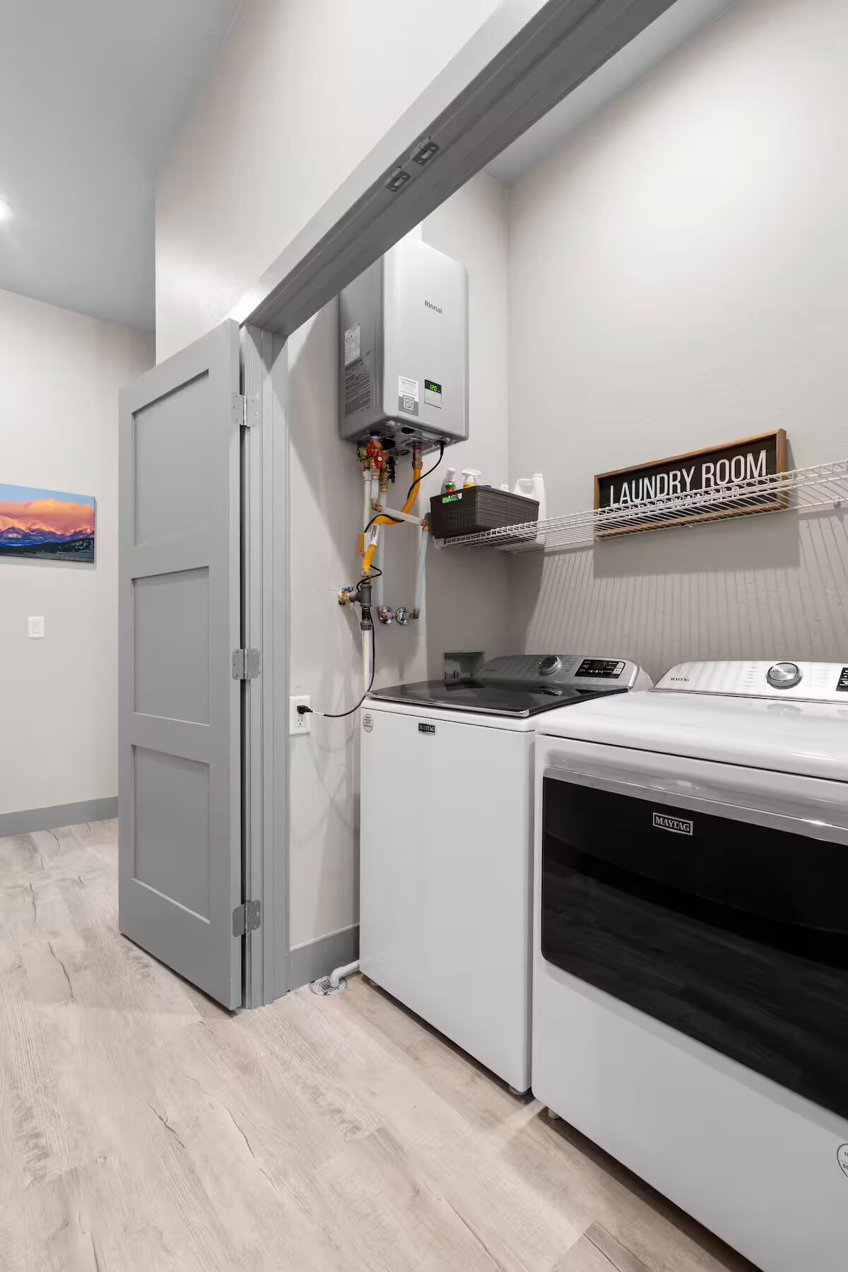 A laundry room with a Maytag washer and dryer, a Rinnai water heater, and a shelf with laundry supplies.