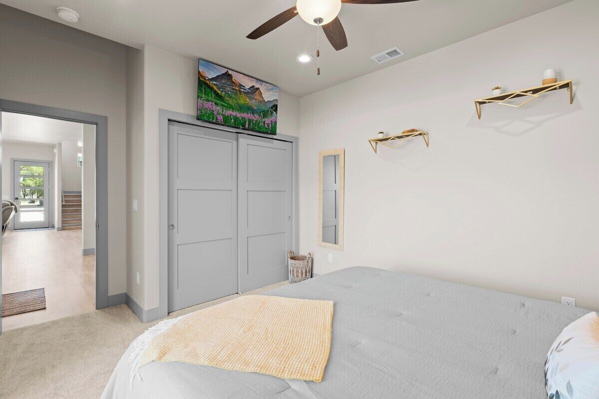 Un dormitorio con cama, ventilador de techo, armario, un cuadro y estantes en la pared.