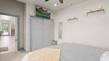 Un dormitorio con cama, ventilador de techo, armario, un cuadro y estantes en la pared.