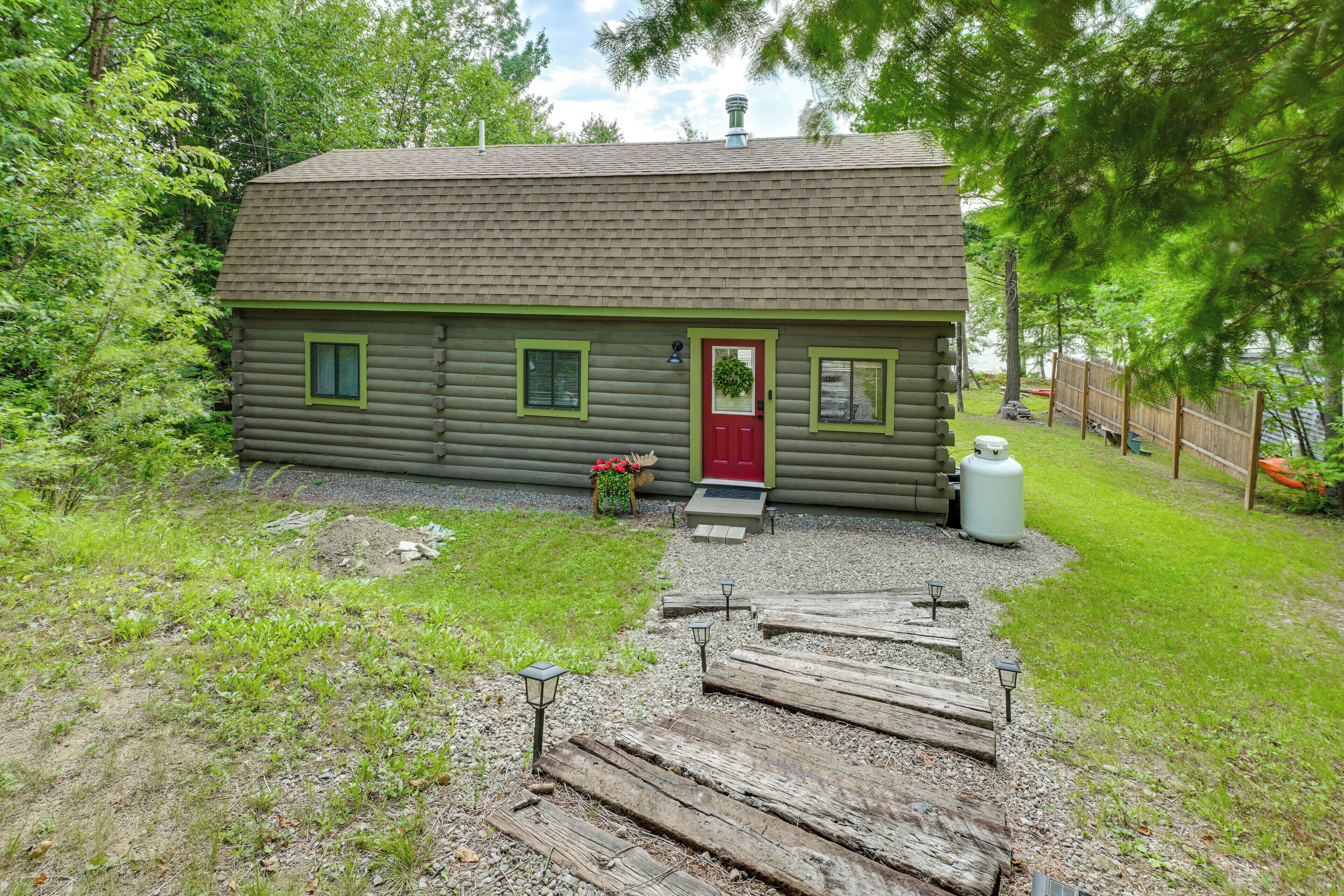 A log cabin with a red door, a small porch, and a gravel pathway leading to the entrance.