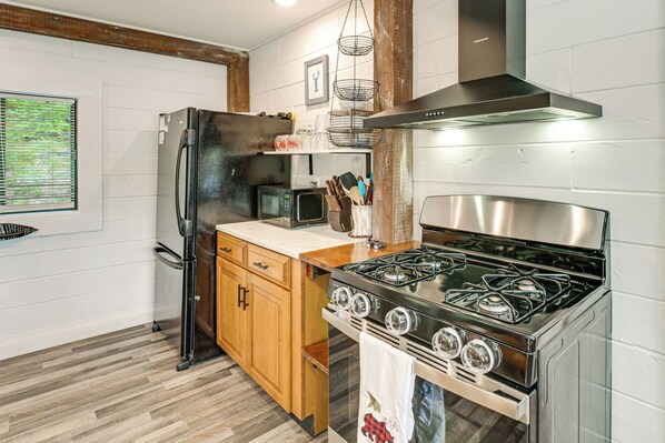 A modern kitchen with a stainless steel stove, a black refrigerator, wooden cabinets, and a microwave.