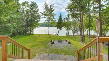 A wooden deck leading to a lakeside view with a fire pit and a thermometer.