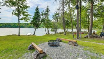 A lakeside outdoor seating area with a fire pit, benches, and a dock.