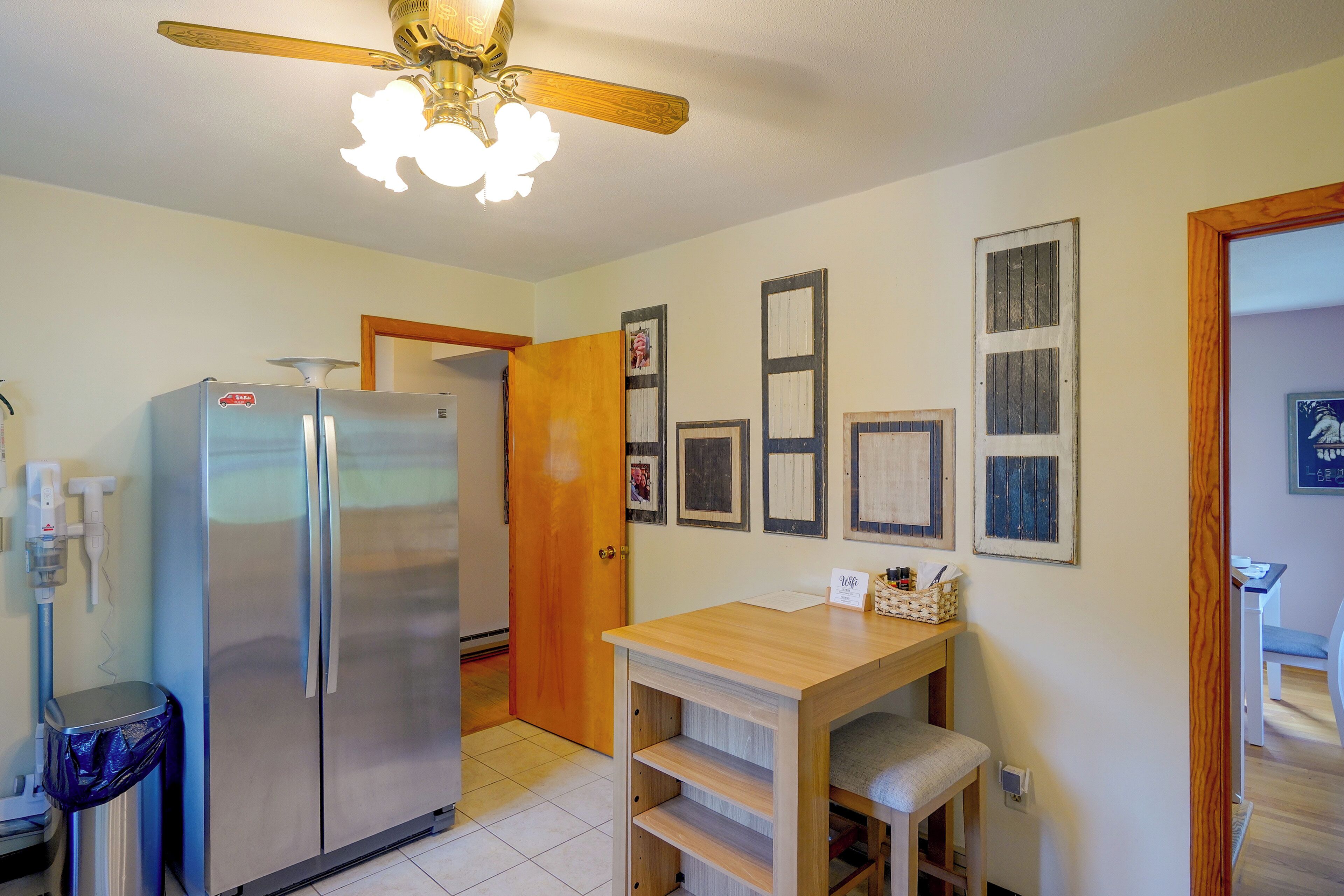 A compact kitchen with a stainless steel refrigerator, a wooden table, and a ceiling fan.
