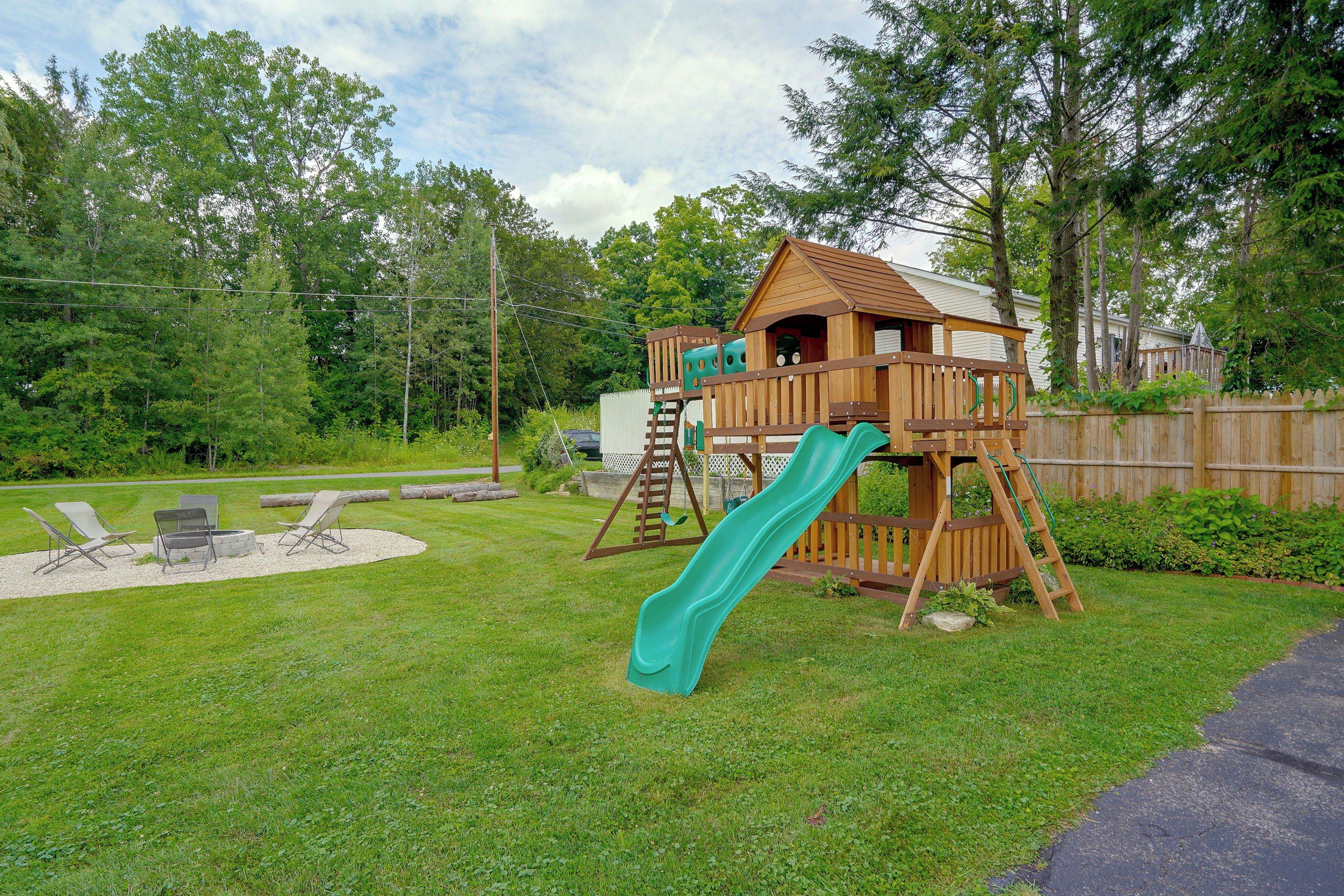 A wooden play structure with a slide, surrounded by a grassy yard and a wooden fence.