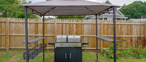 A barbecue grill under a covered pavilion with a wooden fence in the background.