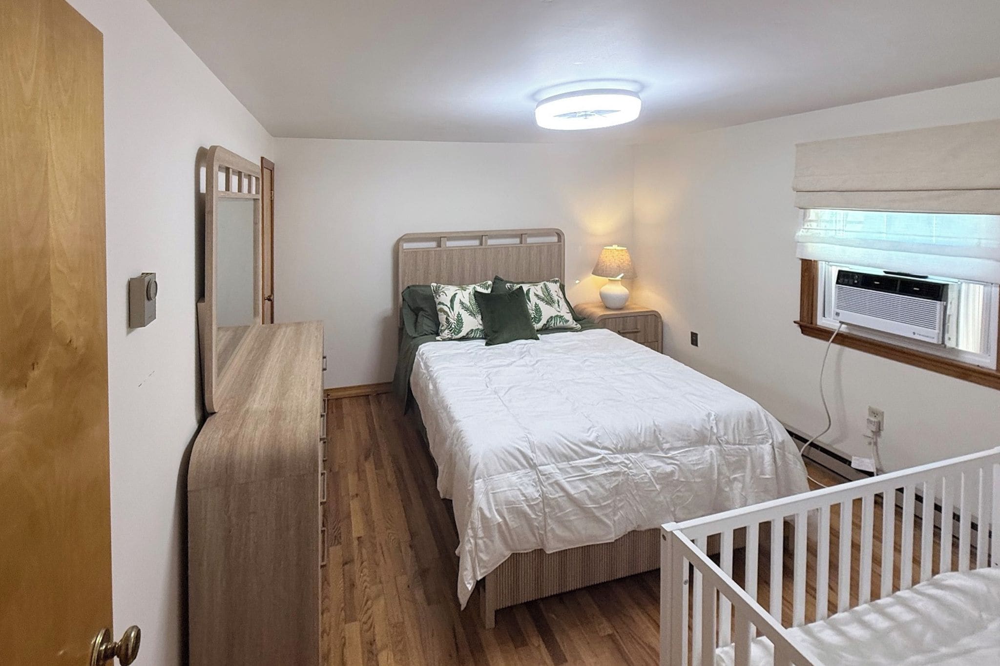 A bedroom with a bed, bedside table, lamp, and an air conditioning unit.