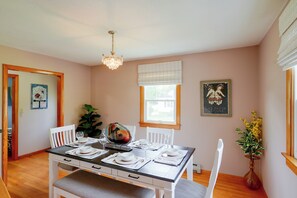 A dining area with a table set for four, chairs, a chandelier, a window with blinds, and a framed picture on the wall.