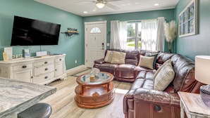 A living room with a television, a white cabinet, a brown leather couch, a glass coffee table, and a ceiling fan. - 2 Nature Coast Units w/ Shared Courtyard (Homosassa)