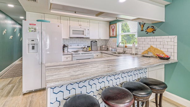 A modern kitchen with white appliances, a marble countertop, and a teal accent wall. - 2 Nature Coast Units w/ Shared Courtyard (Homosassa)