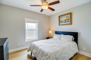 A bedroom with a bed, a ceiling fan, a window with blinds, a bedside table with a lamp, and a framed picture on the wall. - Waterfront Home w/ Deck & Views on Copano Bay! (Taft)