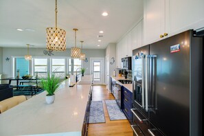 A modern kitchen with a large stainless steel refrigerator, pendant lights, and a view to the outside. - Waterfront Home w/ Deck & Views on Copano Bay! (Taft)