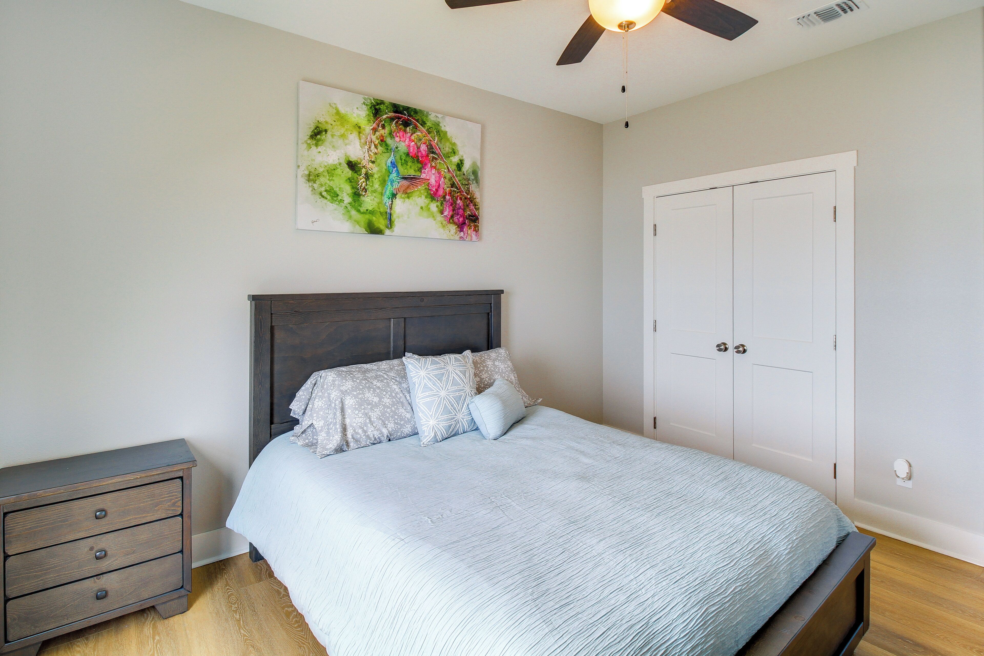 A bedroom with a bed, a nightstand, a ceiling fan, and a door.
