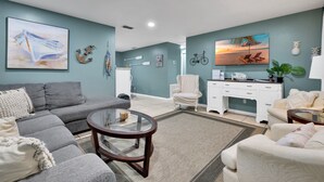 A modern living room with a grey sofa, a round coffee table, and a white armchair. There are two paintings on the walls, one of a boat and another of a beach scene. - 2-home Nature Coast Retreat Near 3 Sisters Springs (Homosassa)